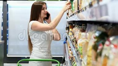 快乐的女人选择<strong>超市</strong>里的产品，用<strong>手机</strong>交谈，顾客选择货架上的商品。
